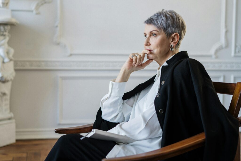 Elderly woman sitting thoughtfully in an elegant indoor setting, showcasing wisdom and contemplation.