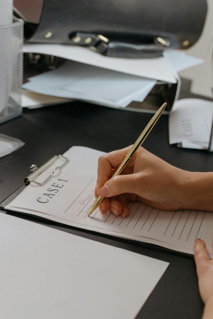 Close-up of a person's hand writing on a case document with a gold pen, emphasizing professionalism.